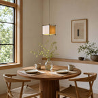 Lit Clérachic cube lantern pendant over a round table set for breakfast, beside a window with a view of green trees.
