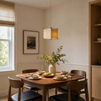 Square-framed Clérachic paper pendant over a wooden dining table set with bowls, plates and a vase of green stems.