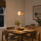 Lit Clérachic cube lantern pendant above a set wooden table with a bowl of fruit and a framed landscape print behind.
