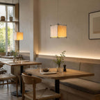 Clérachic paper cube pendant glowing in a cafe-style corner, above small tables and a banquette lit by a strip light.