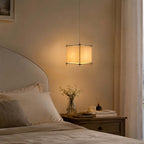 Clérachic paper lantern pendant lit above a wooden nightstand and an upholstered bed with a vase of dried flowers.