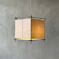 Close view of a Clérachic cube lantern pendant against a grey plaster wall, with paper panels, a stitched seam and a metal frame.