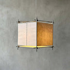 Close view of a Clérachic cube lantern pendant against a grey plaster wall, with paper panels, a stitched seam and a metal frame.