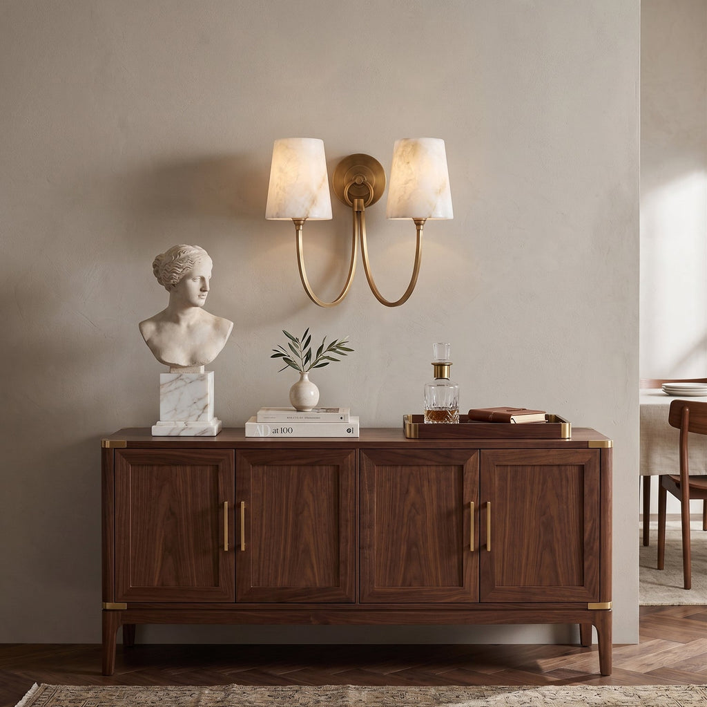 Two-light alabaster sconce from Clérachic above a walnut cabinet, with a marble bust and a small plant on top.