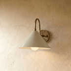 Clérachic cone-shade wall sconce in vintage brass with a gooseneck arm, mounted on a plaster wall in studio light.