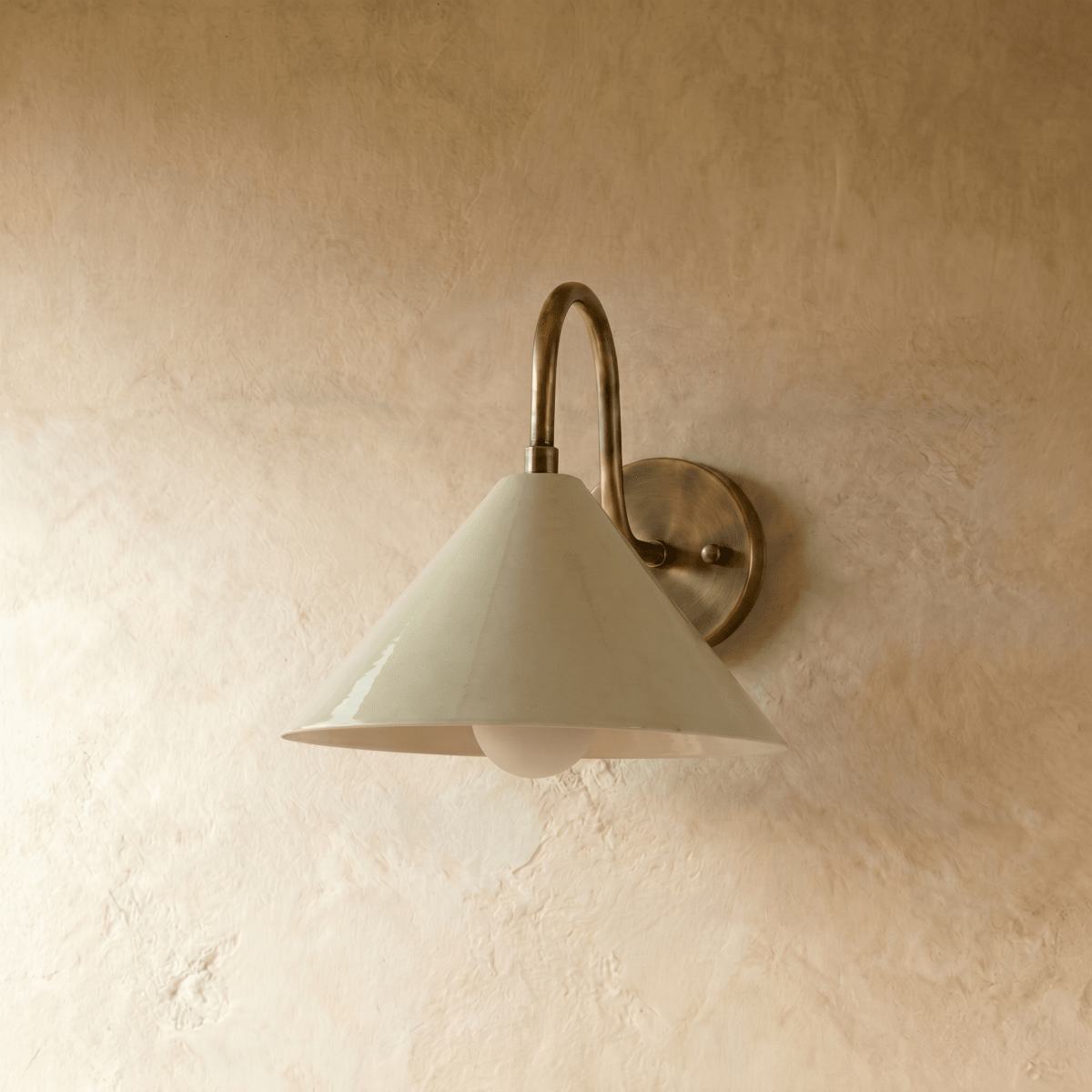 Clérachic cone-shade wall sconce in vintage brass, photographed on a plain plaster wall from a slightly closer angle.