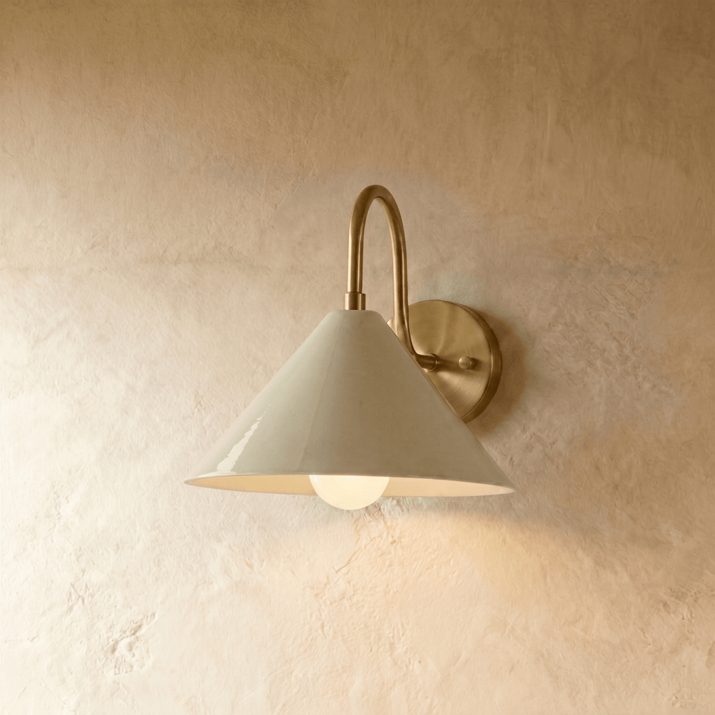 Clérachic cone-shade wall sconce in vintage brass, shown closer-cropped against a plain plaster studio wall.