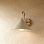 Clérachic cone-shade wall sconce in vintage brass, shown closer-cropped against a plain plaster studio wall.