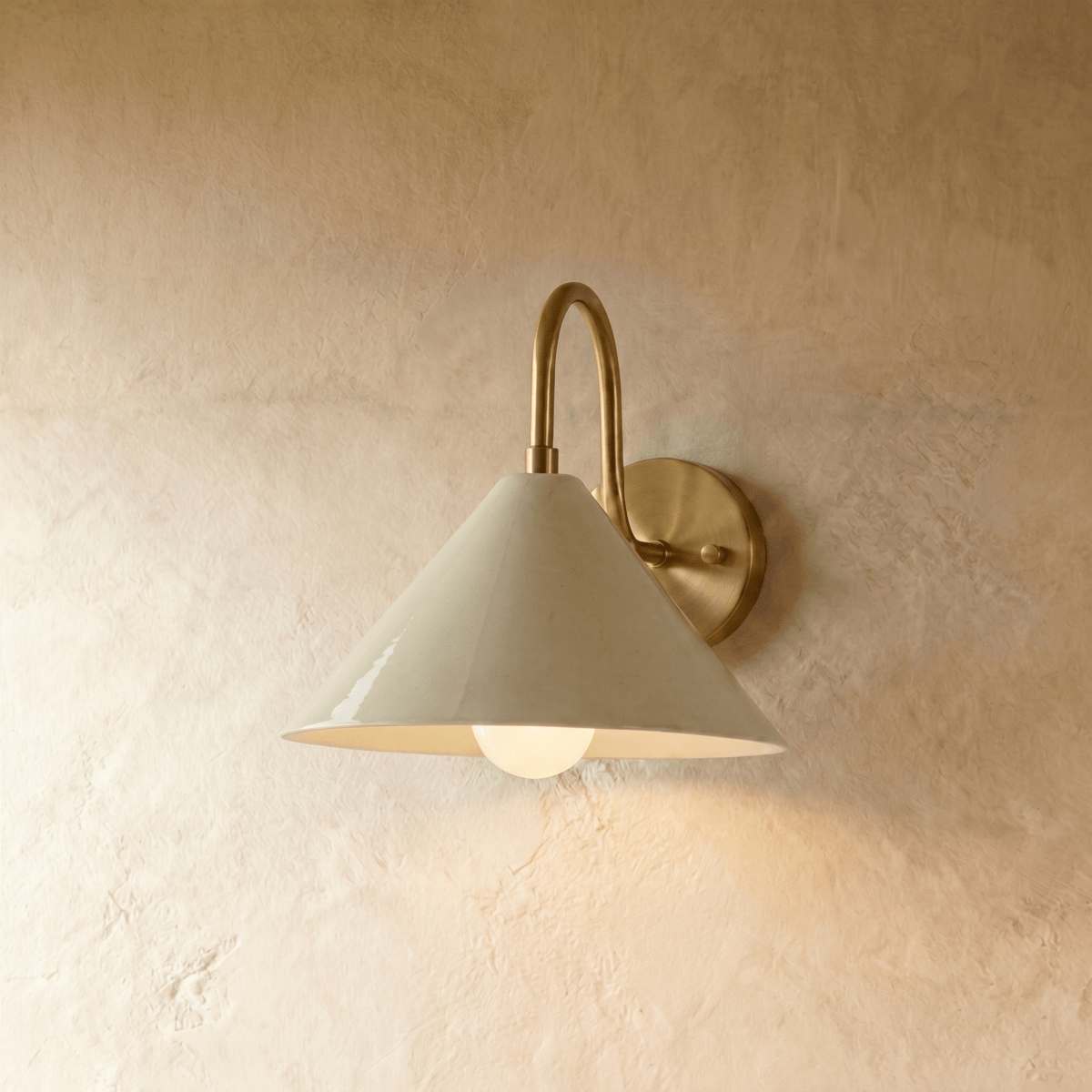 Clérachic cone-shade wall sconce in vintage brass, shown closer-cropped against a plain plaster studio wall.