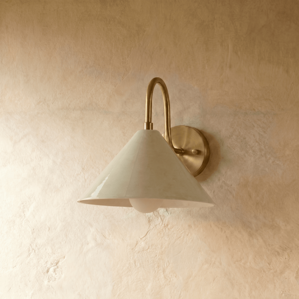 Clérachic cone-shade wall sconce in polished brass with a gooseneck arm, mounted on a plaster wall in studio light.