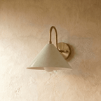 Clérachic cone-shade wall sconce in polished brass with a gooseneck arm, mounted on a plaster wall in studio light.