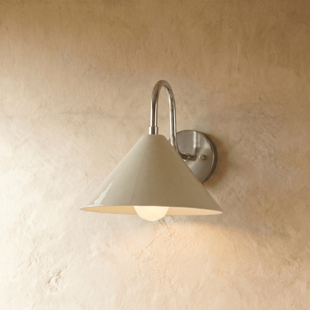 Clérachic cone-shade wall sconce in chrome with a curved gooseneck arm, mounted on a plaster wall in studio light.