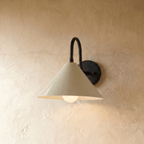 Clérachic cone-shade wall sconce in matte black with a gooseneck arm, mounted on a plaster wall in studio light.