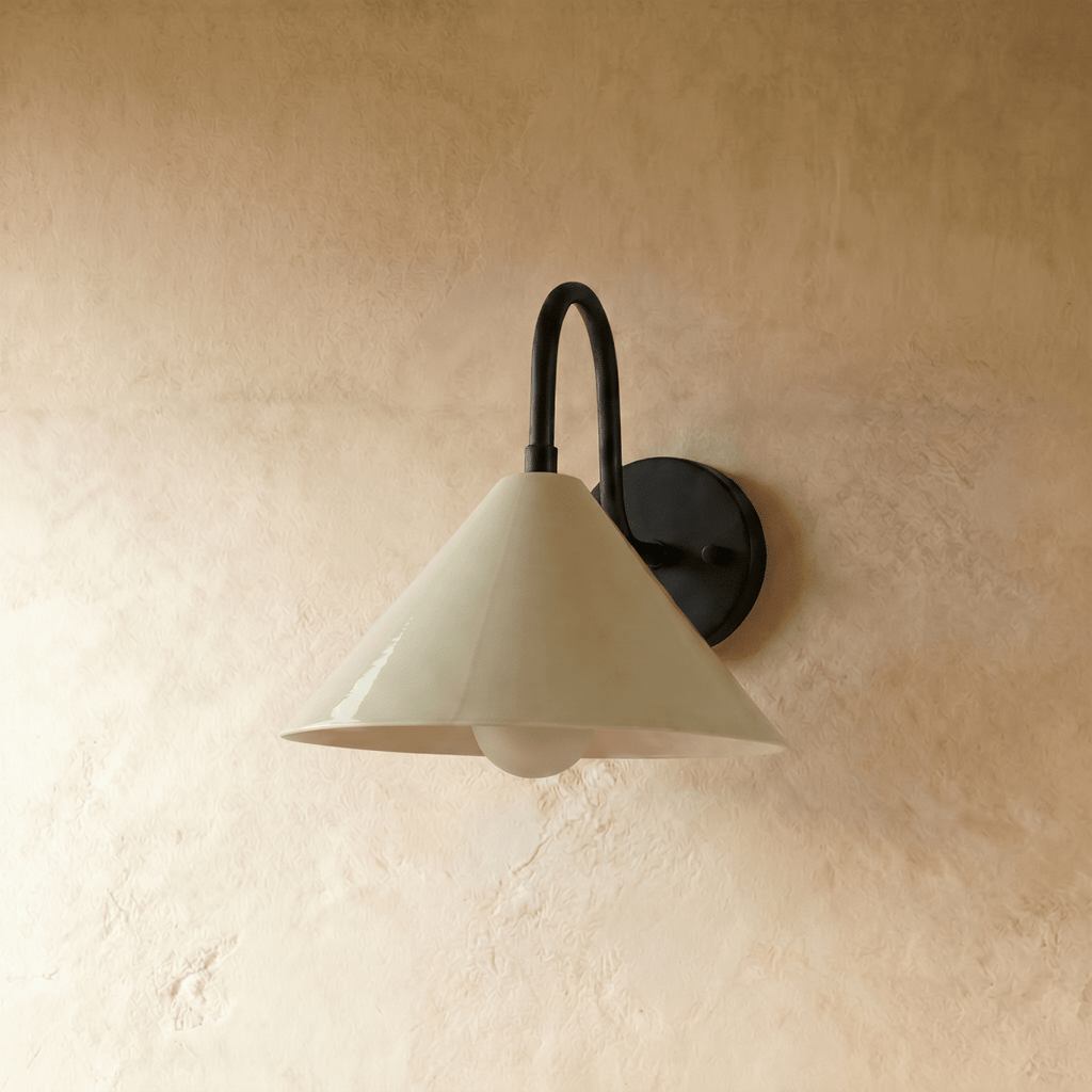 Clérachic cone-shade wall sconce in matte black, shown closer-cropped against a plain plaster studio wall.