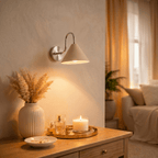 Clérachic chrome cone-shade wall sconce lit above a side table with dried pampas grass and a lit candle.