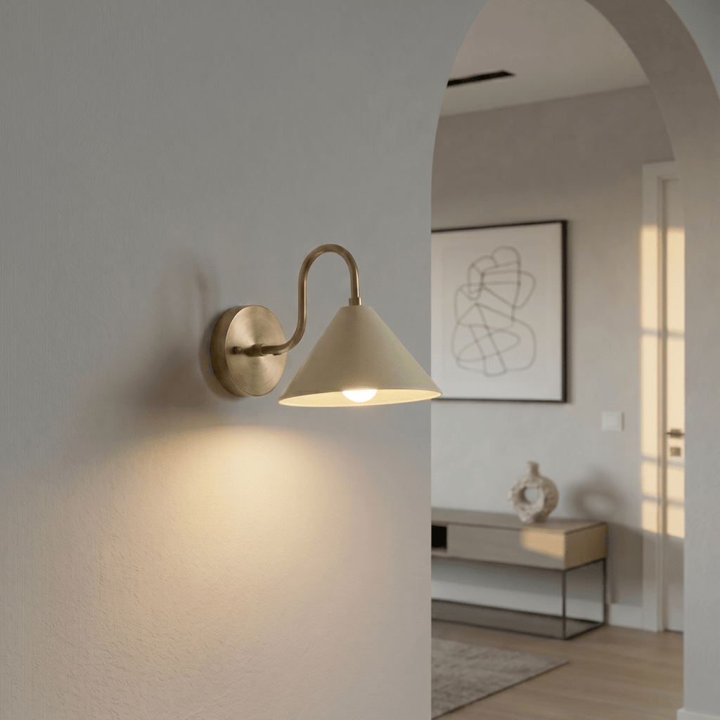 Clérachic vintage brass cone-shade wall sconce lit on a hallway wall beside an archway into a living room.