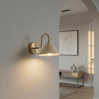 Clérachic vintage brass cone-shade wall sconce lit on a hallway wall beside an archway into a living room.