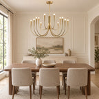 A brass-toned Clérachic chandelier above a long walnut dining table with cream upholstered chairs, in a panelled room with tall windows.