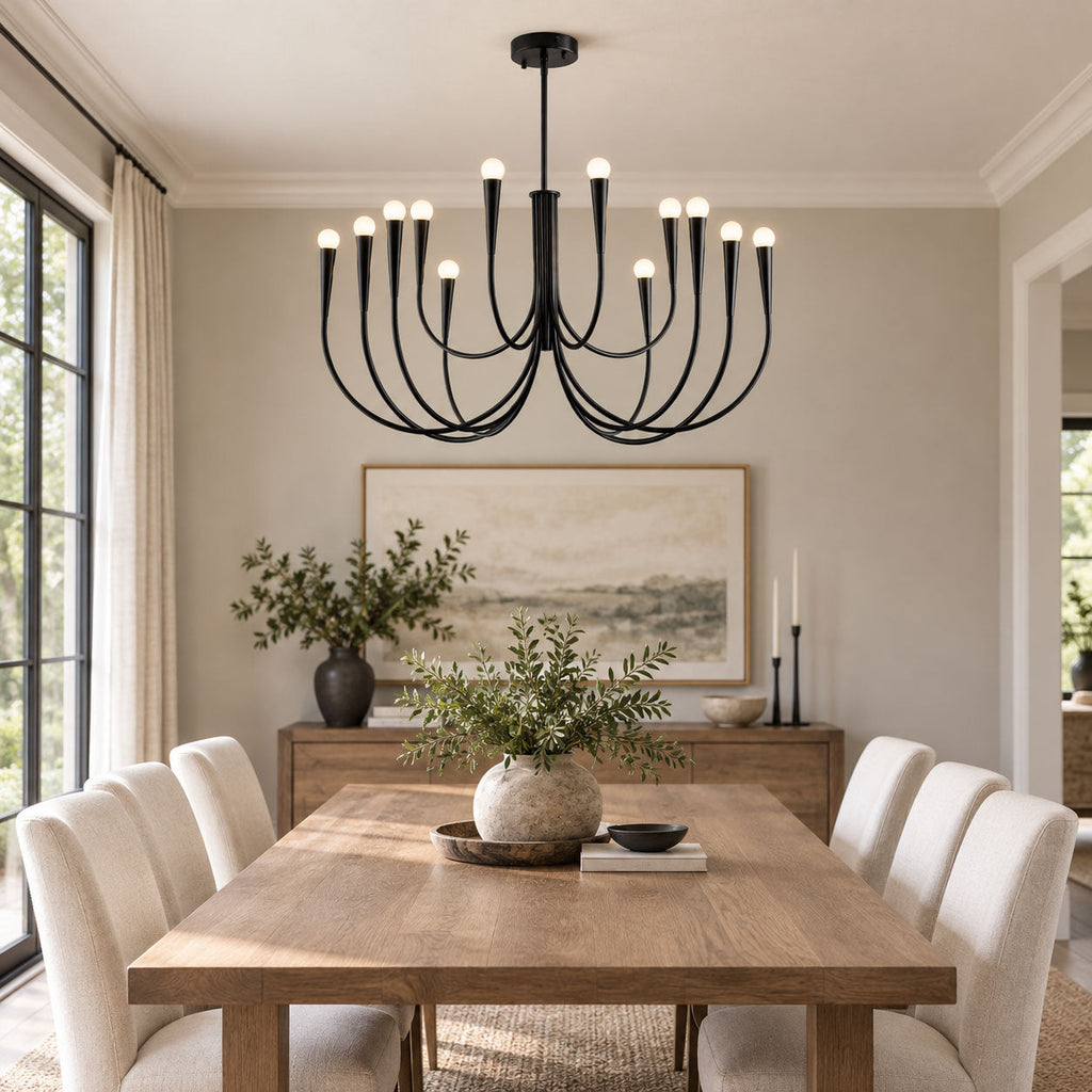 A black Clérachic chandelier with curved arms above a pale wooden dining table, in a grey room with a leafy centrepiece.