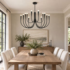 A black Clérachic chandelier with curved arms above a pale wooden dining table, in a grey room with a leafy centrepiece.