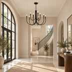 A black Clérachic chandelier in an entrance hall with arched glazed doors, a curved staircase and a wooden console table.