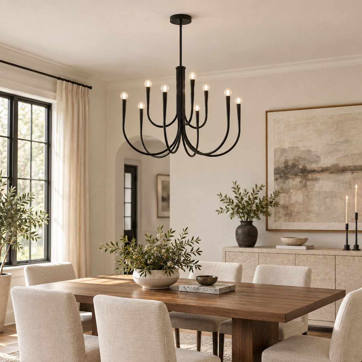 Black Clérachic chandelier above a dining table with cream chairs, beside a tall window and a large landscape painting.