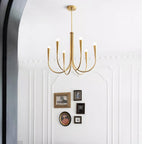 A smaller Clérachic chandelier with brass-toned arms against a white panelled wall, with a cluster of framed pictures below it.