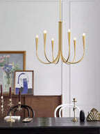 Brass-toned Clérachic chandelier with bare bulbs, hung in front of a wood sideboard and a table with candlesticks and framed art.