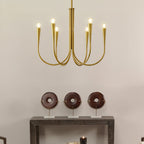 A Clérachic chandelier with brass-toned arms and conical sockets above a dark console table with three round wooden ornaments.