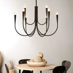 Close view of a black Clérachic chandelier with looping arms, above a round wooden table with a bowl of decorative balls.