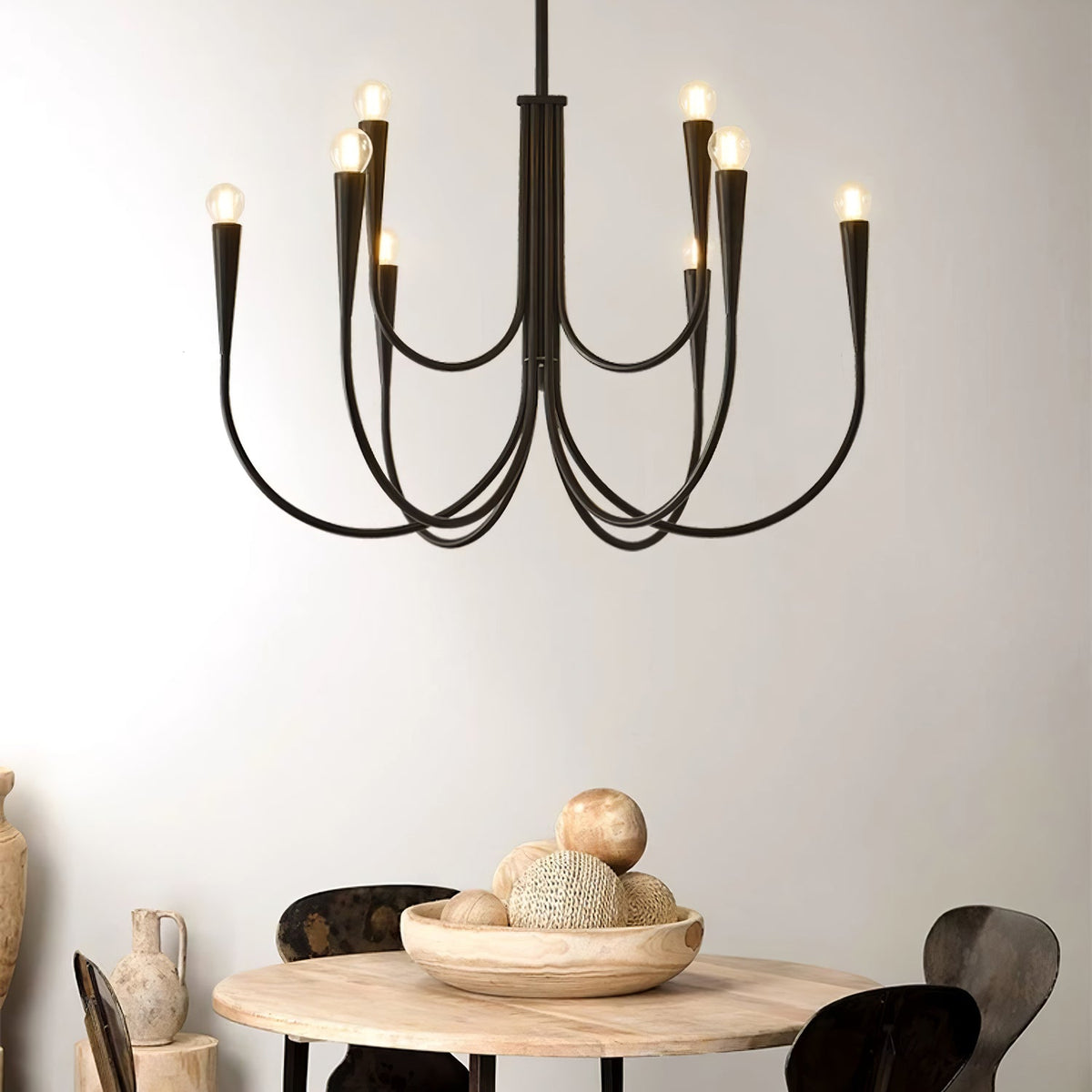 Close view of a black Clérachic chandelier with looping arms, above a round wooden table with a bowl of decorative balls.