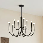 A black Clérachic chandelier with a stepped, two-tier arm layout, hung against a cream wall with a clock partly visible below.