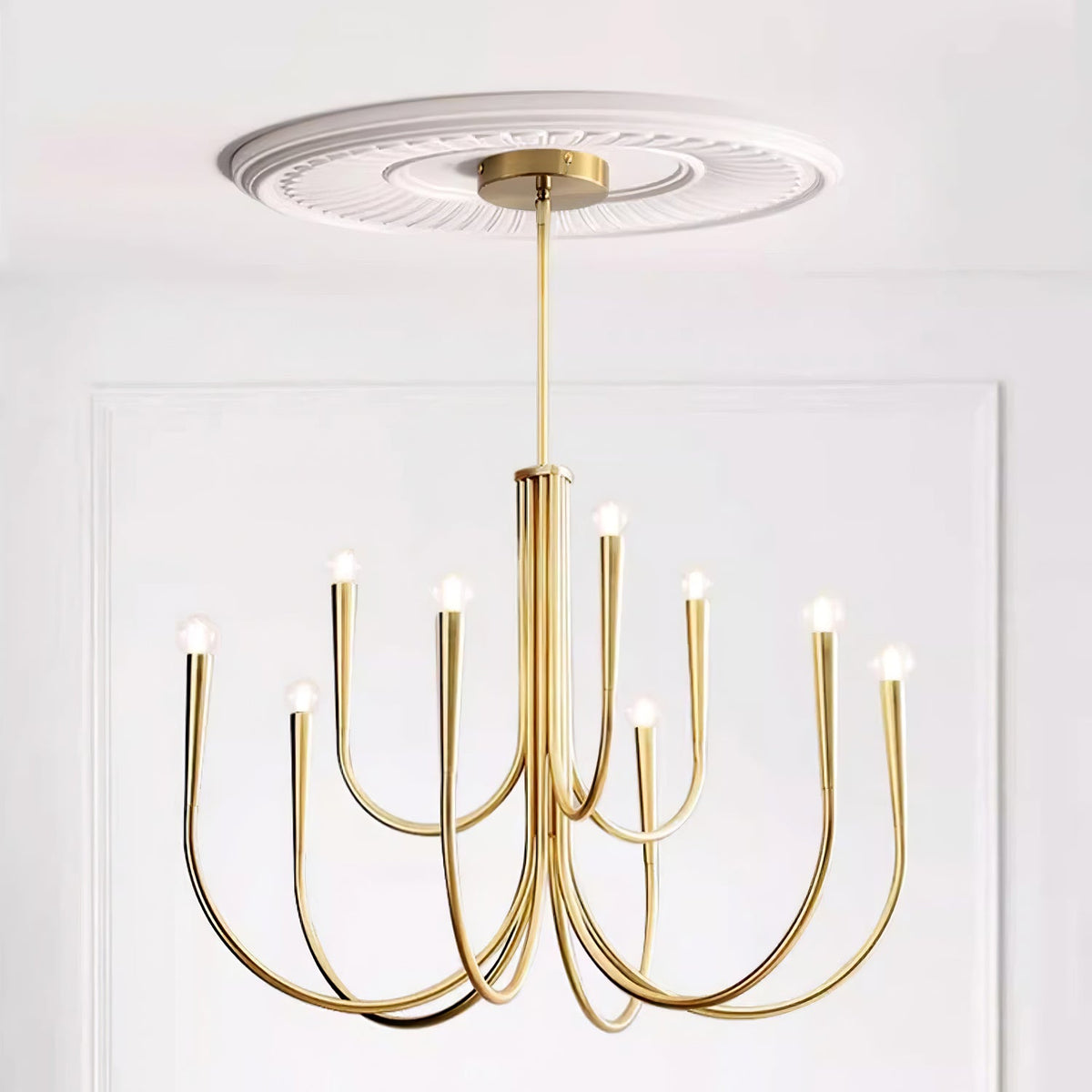 Brass-toned Clérachic chandelier under a carved white ceiling rose, with arms curving out and up to bare bulbs.