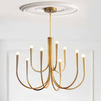 A Clérachic chandelier with a brass-toned finish, hung from a plaster ceiling rose against white panelled walls.