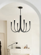 A black Clérachic chandelier in an arched white room, above a mantel with a desk lamp and small ornaments.