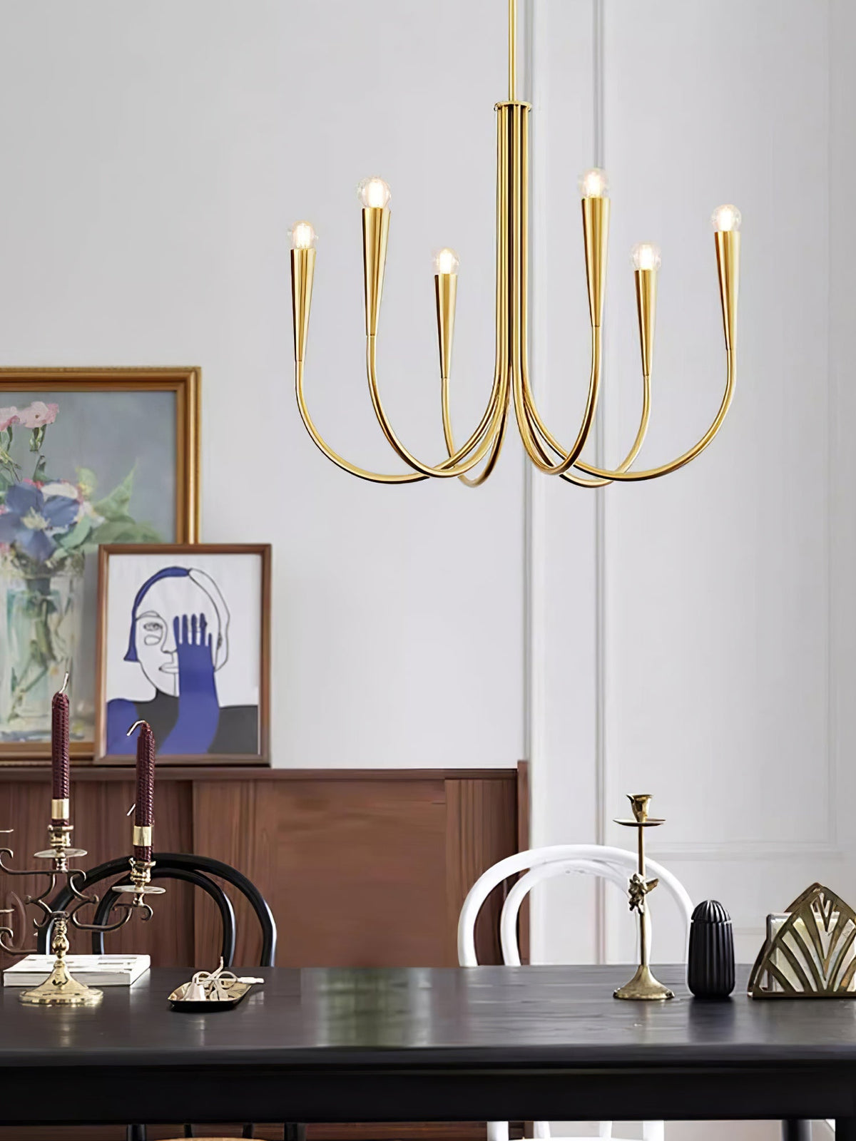 A smaller brass-toned Clérachic chandelier above a black table with candlesticks, a framed print and a wooden sideboard.