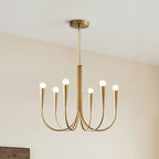 Brass-toned Clérachic chandelier with six arms and a rod, hung against a cream wall with the corner of a wooden frame below.