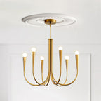A brass-toned Clérachic chandelier with a white ceiling rose above it, against a white panelled wall.