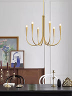 Brass-toned Clérachic chandelier with six arms, hung in front of a white wall with a dark wooden bureau and a framed painting.