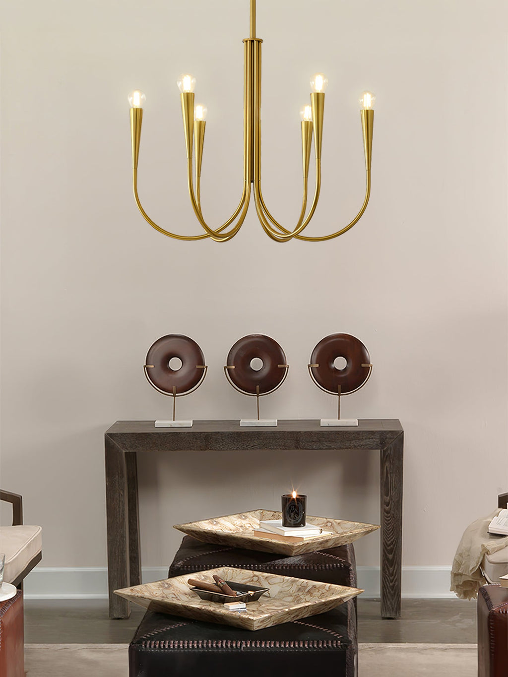 Small brass-toned Clérachic chandelier with six arms, seen against a warm wall with a console table and ornaments below.