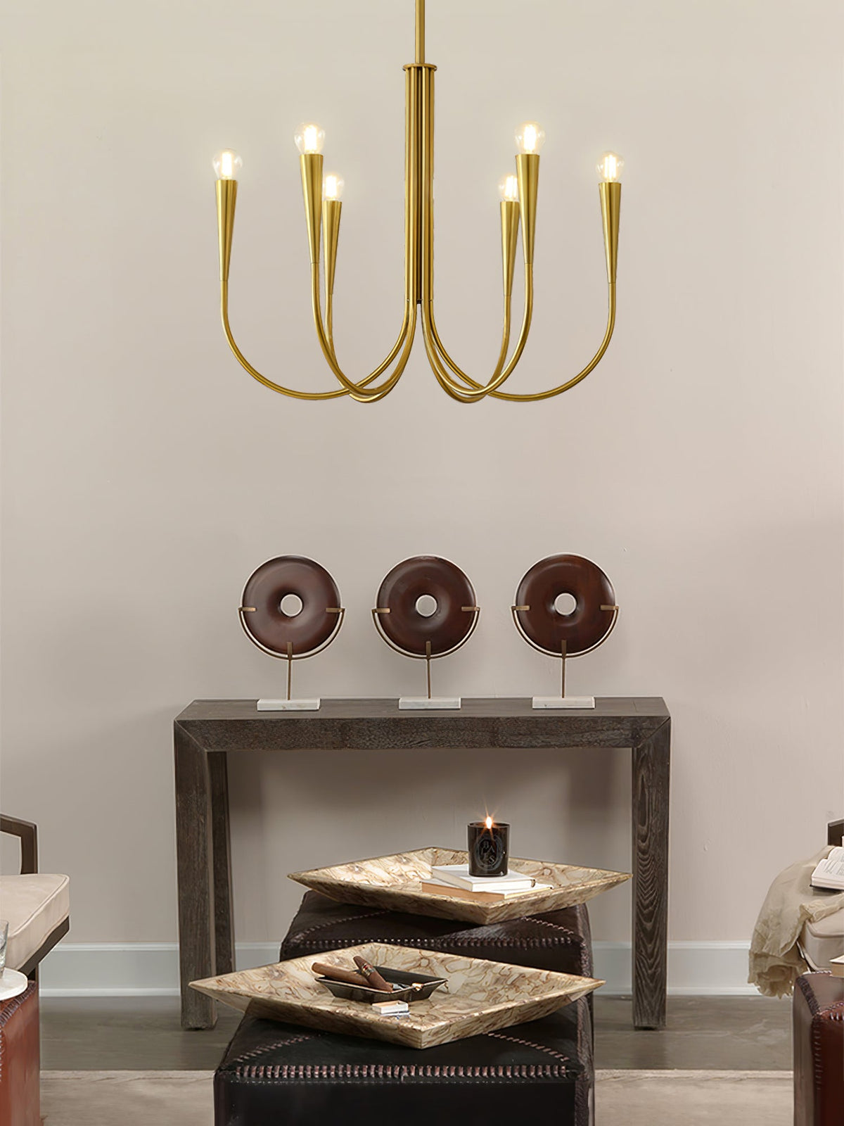 Small brass-toned Clérachic chandelier with six arms, seen against a warm wall with a console table and ornaments below.