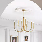 A Clérachic chandelier in a brass tone, with two tiers of arms, hung under a plaster rose in an arched room with framed art.