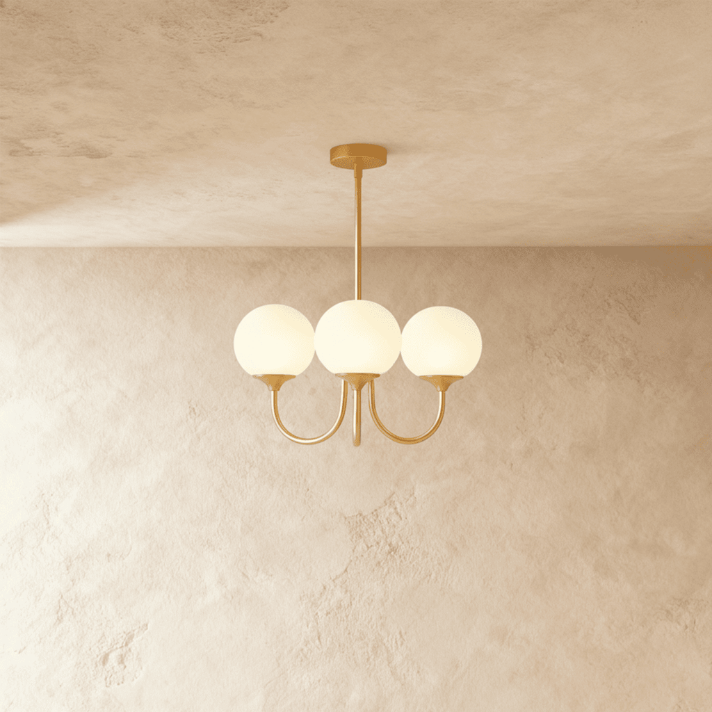 Clérachic three-light chandelier with white glass globes on curved brass-toned arms, hung from a rod against a limewash wall.