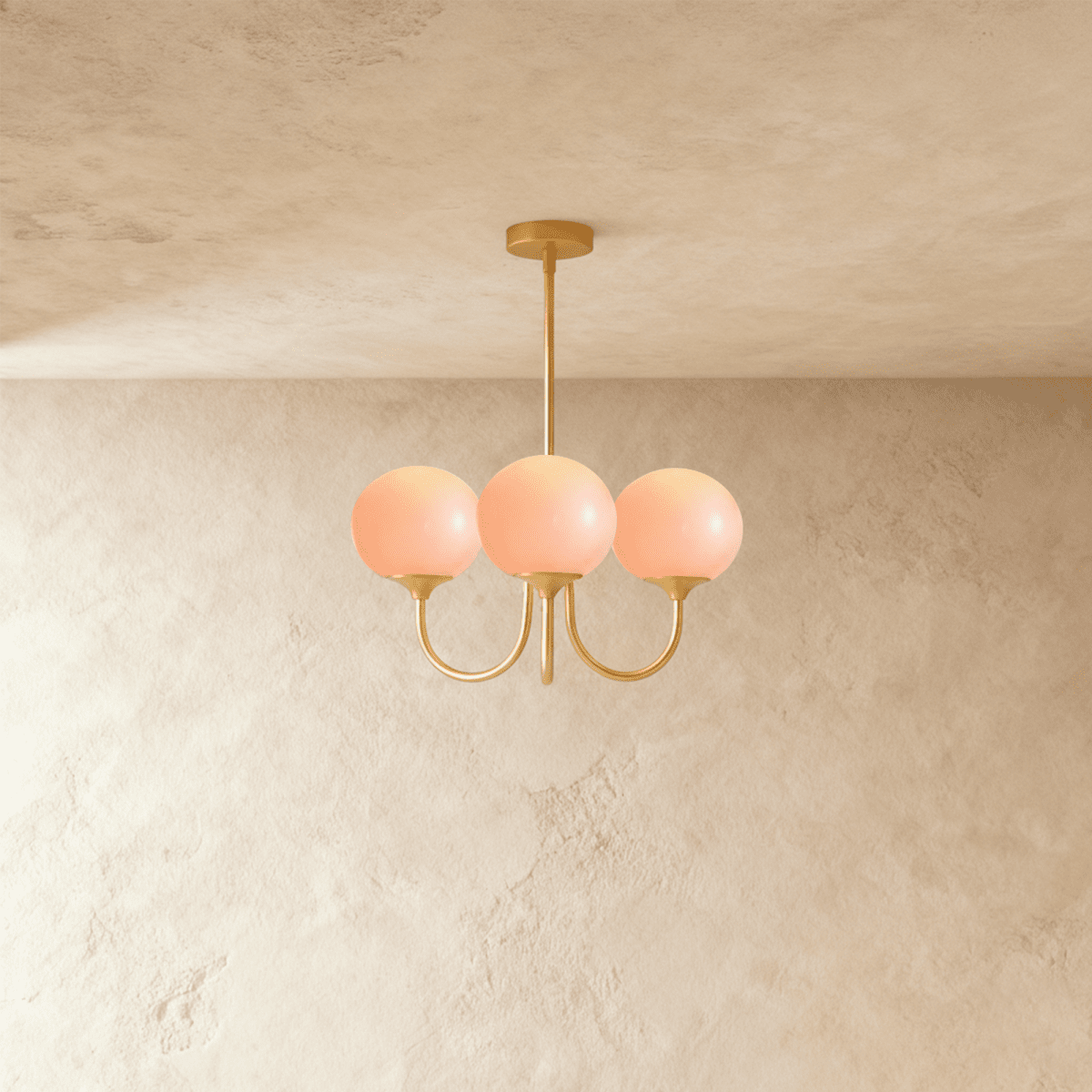 Clérachic three-light chandelier with pale pink glass globes lit warm on curved brass-toned arms and a slim ceiling rod.