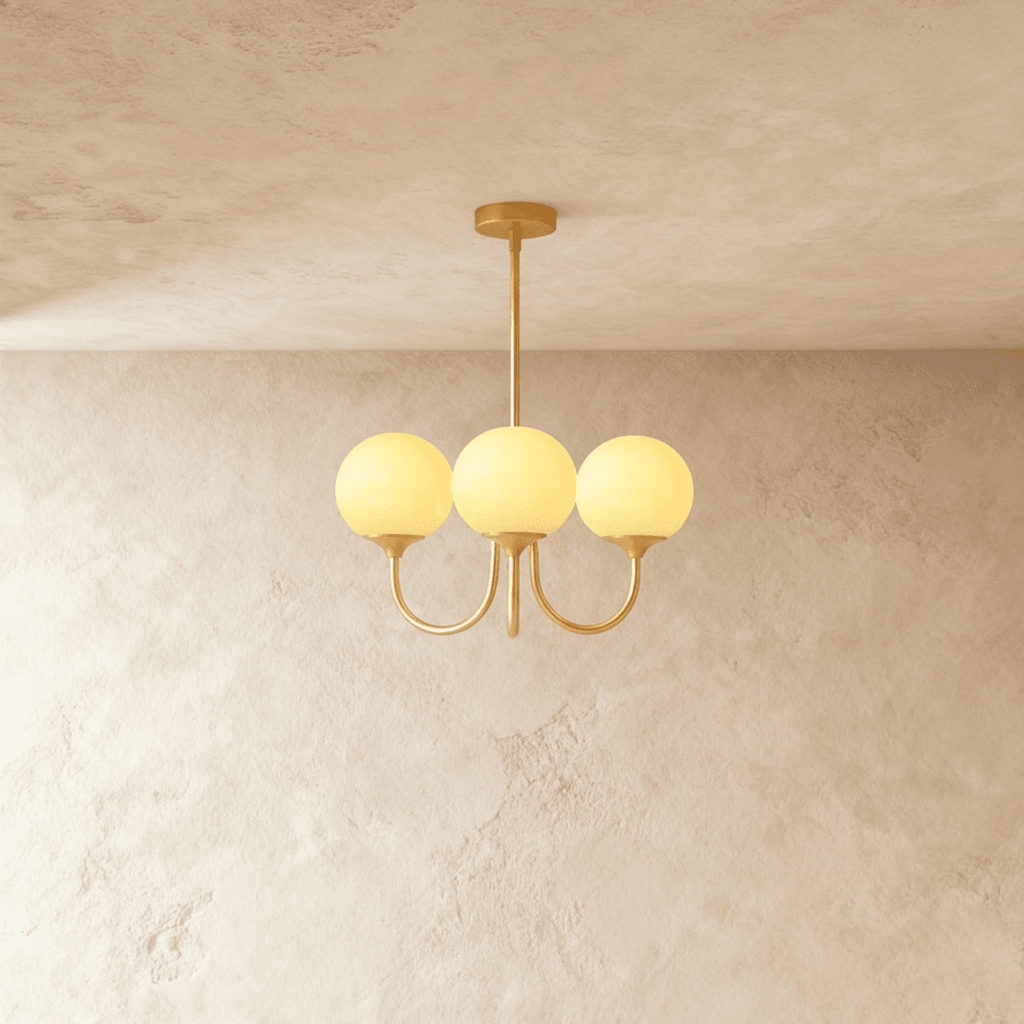 Clérachic three-light chandelier with softly lit butter-yellow glass globes on curved brass-toned arms and a slim stem.