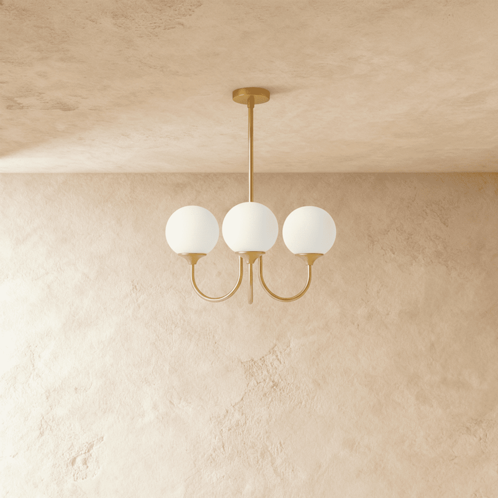 Clérachic three-light chandelier with unlit white glass globes on curved brass-toned arms, shown against a limewash wall.