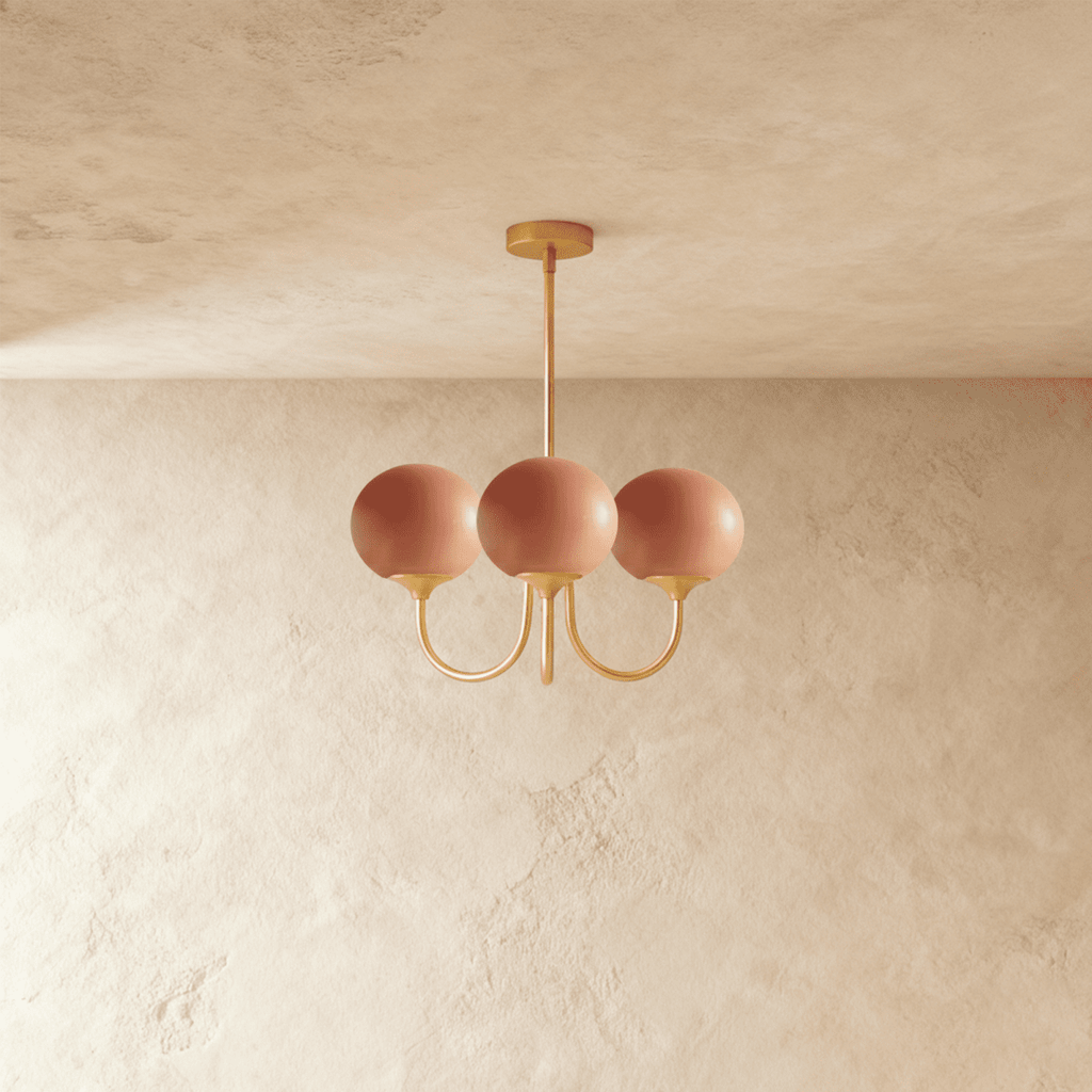 Clérachic three-light chandelier with terracotta-pink glass globes on curved brass-toned arms hanging from a slim rod.