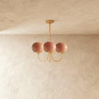 Clérachic three-light chandelier with terracotta-pink glass globes on curved brass-toned arms hanging from a slim rod.