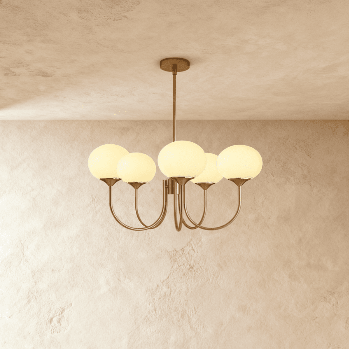 Clérachic five-light chandelier with softly glowing cream oval glass shades on sweeping bronze-toned arms, limewash wall behind.