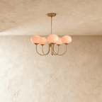 Clérachic five-light chandelier with blush-pink oval glass shades lit warm on curved bronze-toned arms and a slim stem.
